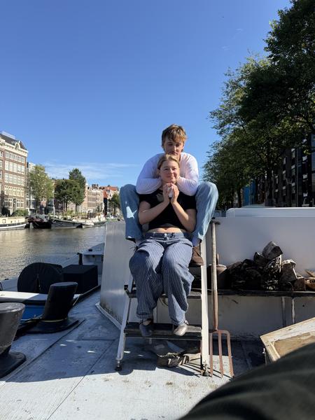 This photo captures two people sitting on a ladder on a boat deck under a clear blue sky in Oudeschans, Uilenburg, Amsterdam